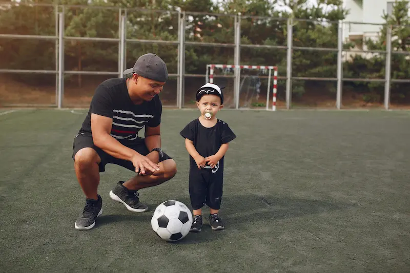 Parent et enfant sur terrain de football – Cela symbolise l'accompagnement parental pour soutenir un jeune sportif